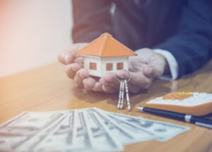 man holding model house and keys with money for loan on desk
